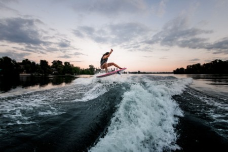 Woman jumping over splashing wave on surf style wakeboard.