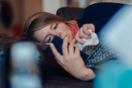 Woman with cold using mobile phone in bed
