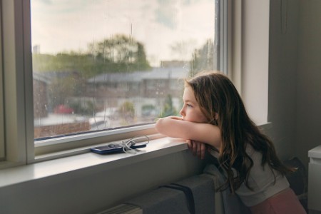
            primer plano de una joven mirando por la ventana en un día de lluvia
        