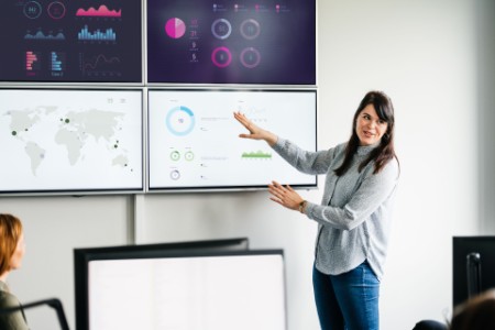 Businesswoman explaining graphs and data displayed on large monitors