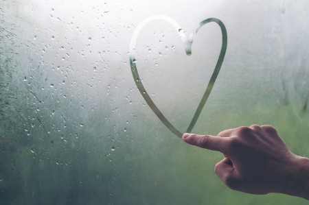 Hand drawing heart on window during rain