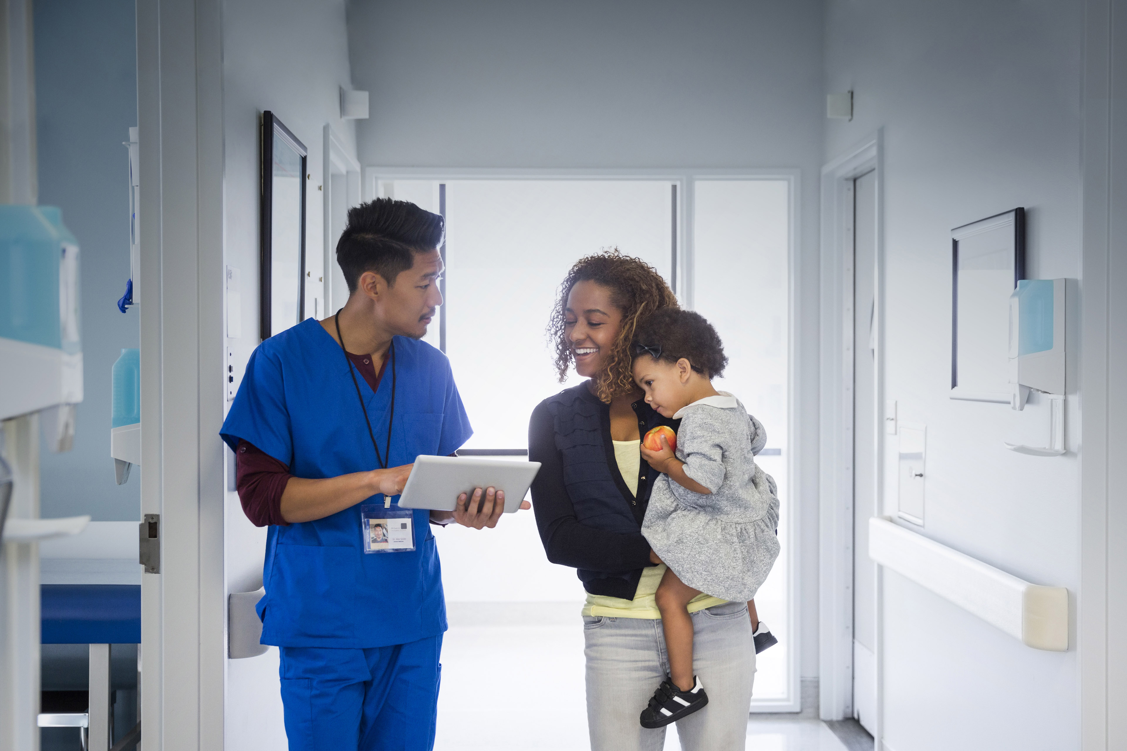 Male nurse talking with mother and baby daughter in hospital corridor
