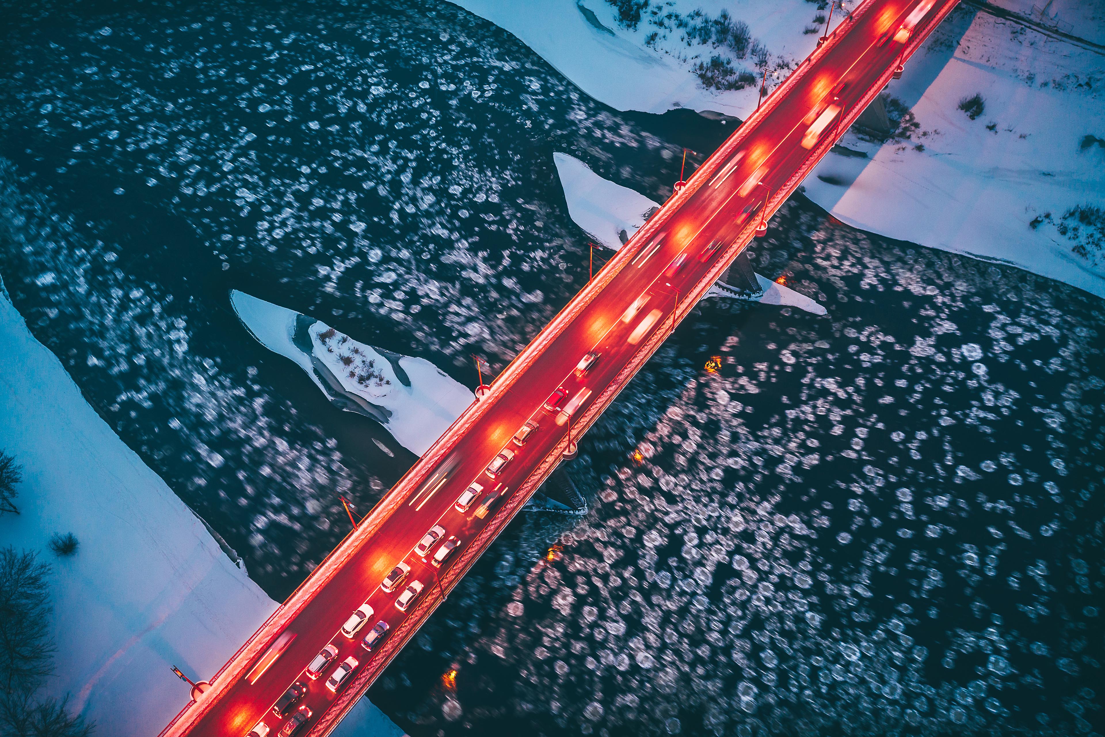 Des reflets de phares de voitures sur un pont, la nuit, au‑dessus d’une rivière gelée