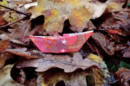 
            Barco de papel hecho con dinero doblado sobre un lecho de hojas
        