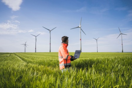 Engineer with laptop in field looking at wind turbines