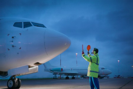 Airport worker guiding aircraft on runway at night