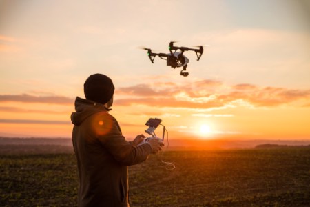 Homem operando um drone com controle remoto ao pôr do sol