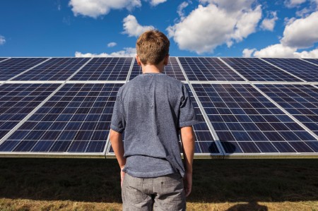 Boy stands in front of blue solar panels