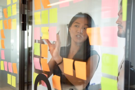 Colleagues working using attached colorful post it notes on glass