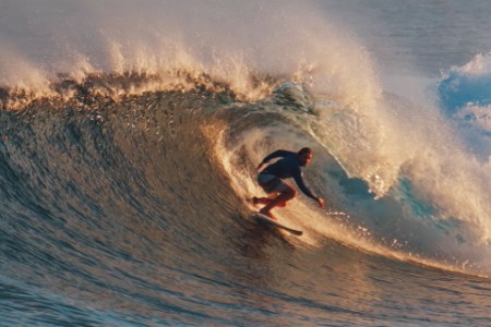 Surfer rides the powerful ocean wave at sunset