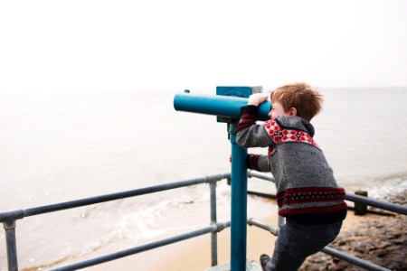 Niño mirando a través de los binoculares en la costa