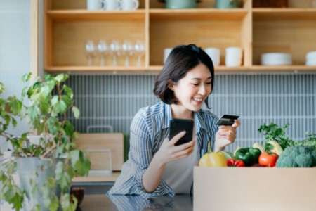 Sorridente jovem mulher asiática compras on-line com celular