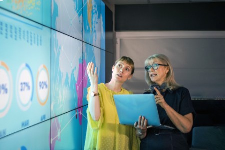 Mujeres empresarias discutiendo ideas frente a un muro con gráficos e información