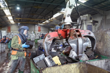バッテリーリサイクル工場で、車載バッテリーを集積容器に投入しようとしている防護服姿の作業員