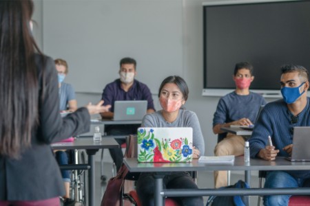 Young adults with masks and laptops in classroom