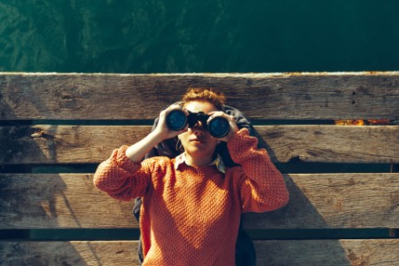 Chica joven en el muelle mirando a través de binoculares