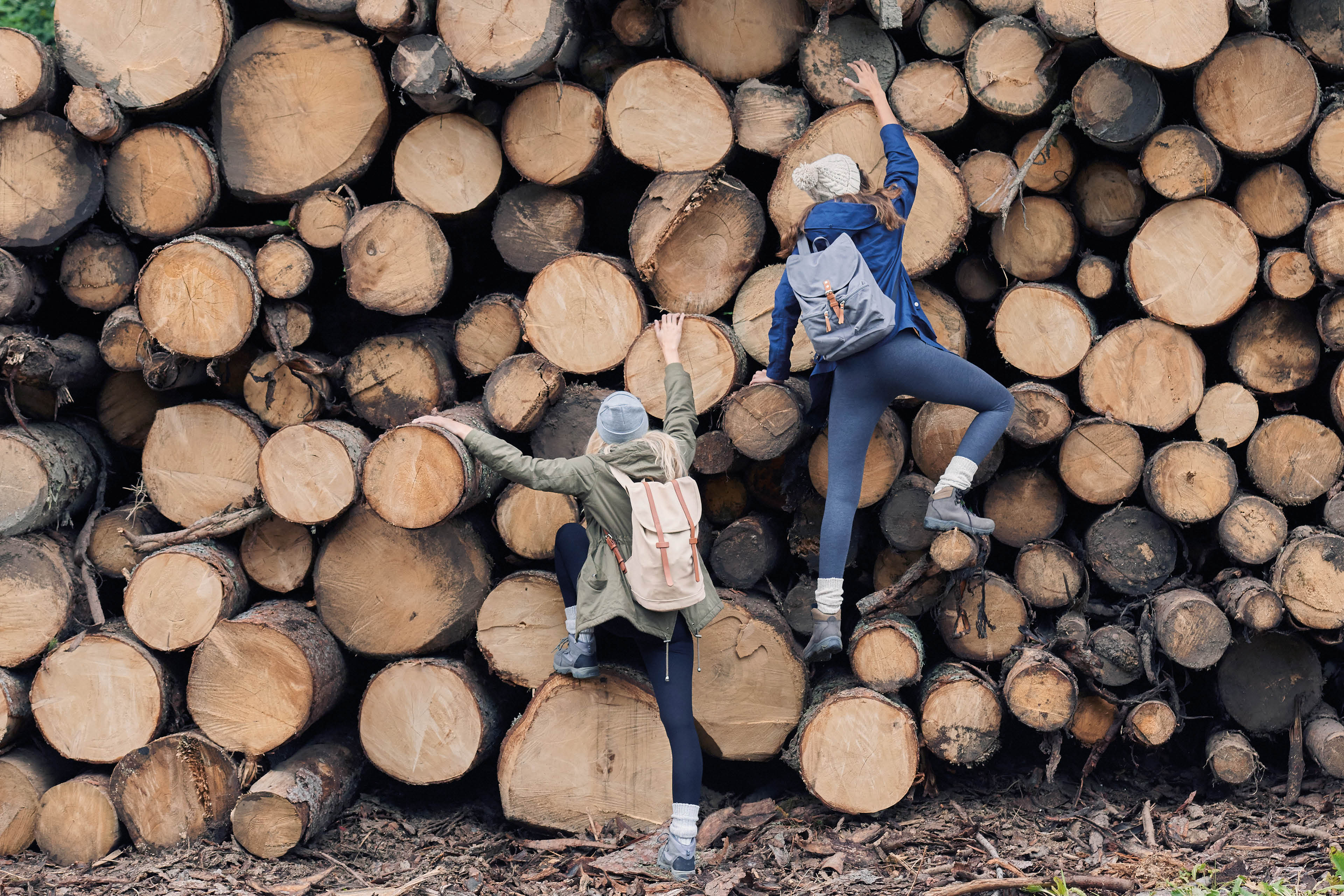 Adventure girl friends having fun climbing up wood pile in forest