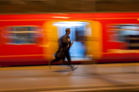 A man runs past a bright orange train to catch a train