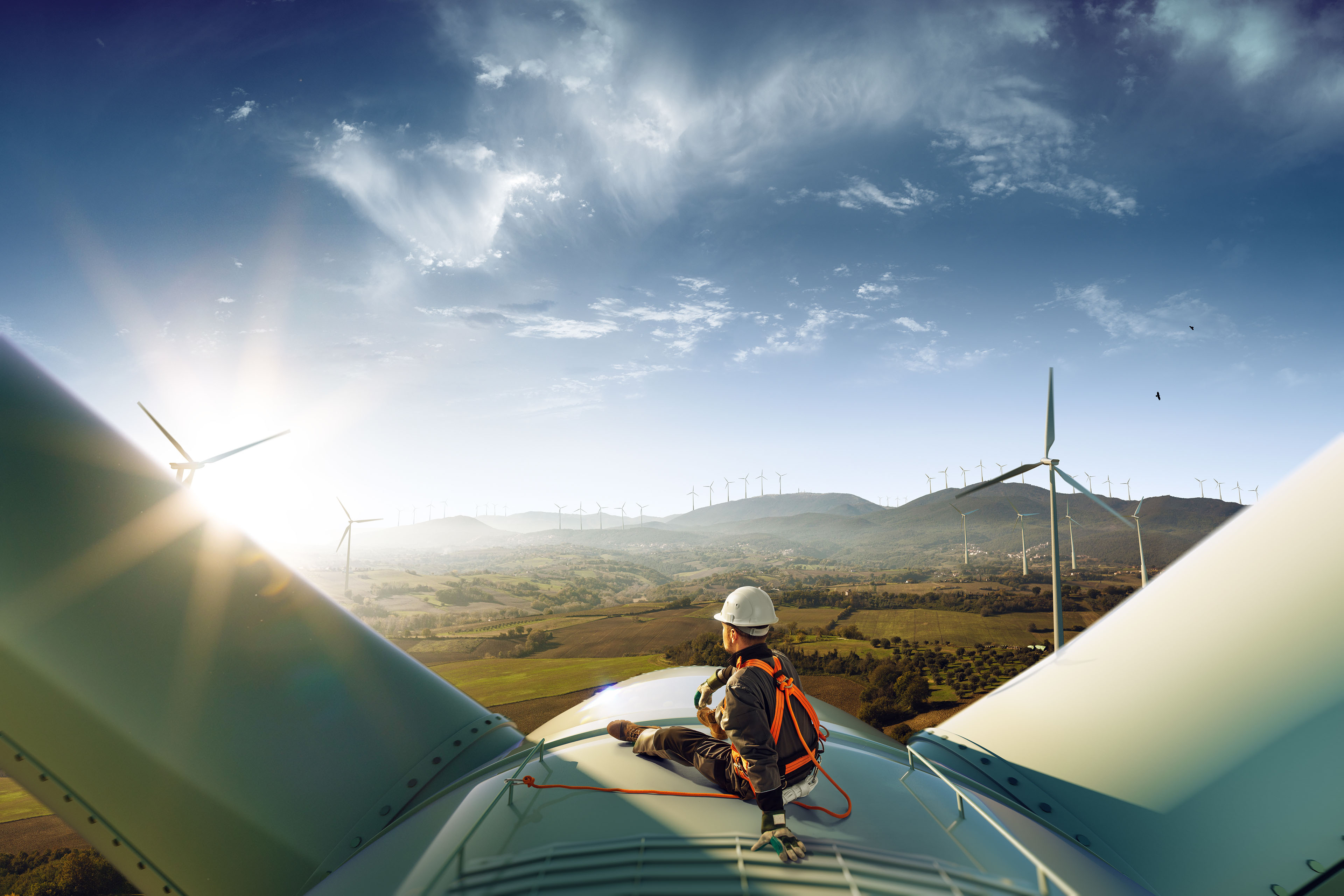 Engineer sitting on top of a wind turbine looking at the sunset