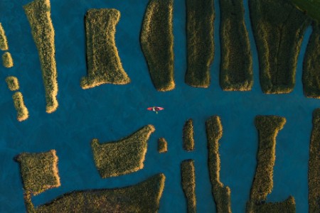 Aerial shot of kayak navigating between grassy patches of land