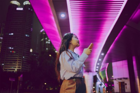Mujer con smartphone en la mano bajo un puente peatonal muy iluminado