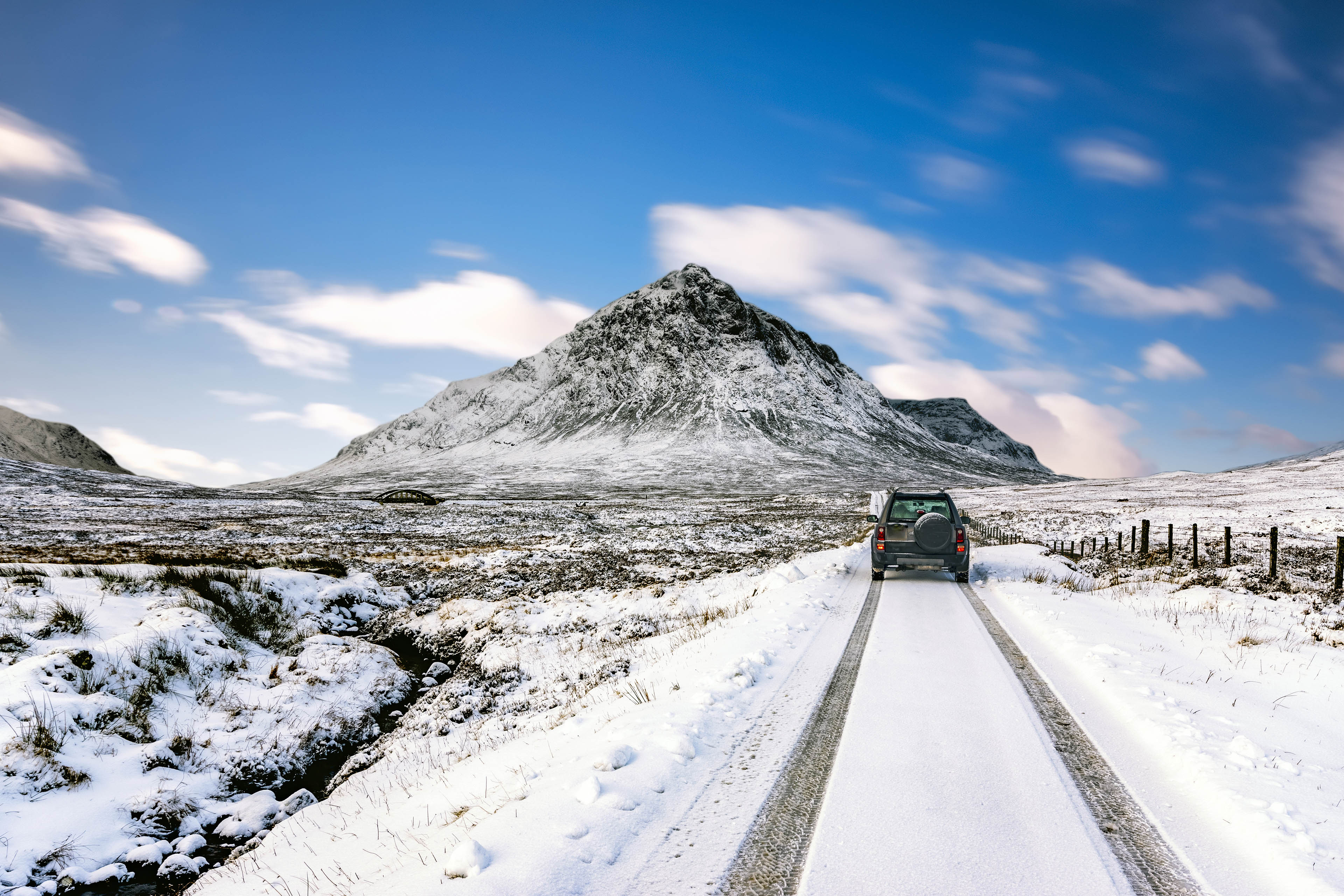 
            Automóvil transitando por camino nevado cerca de montañas
        