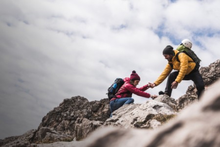 
            Hombre ayudando a una mujer a escalar una roca
        