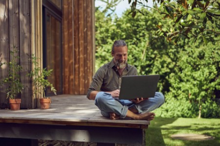 Mature man using laptop while sitting against tiny house