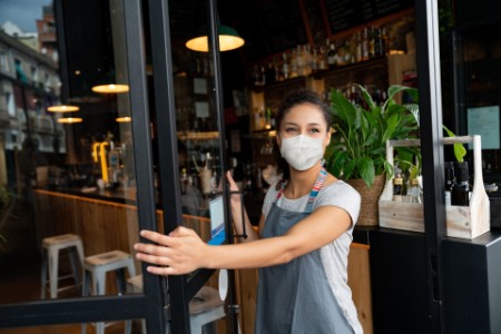 Business owner opening the door at a cafe wearing a facemask