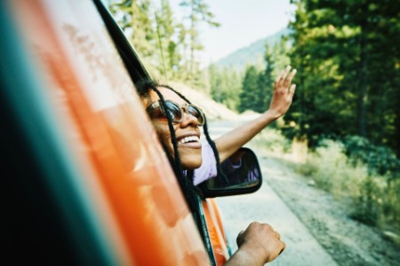 Sorridente mulher cabeça mão mão fora da janela do carro apreciando a vista montanhas
