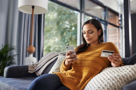 A women on relaxing on the couch with her cellphone and credit card