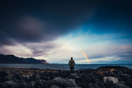 
            Mulher a observar o arco-íris sobre uma paisagem da Islândia
        
