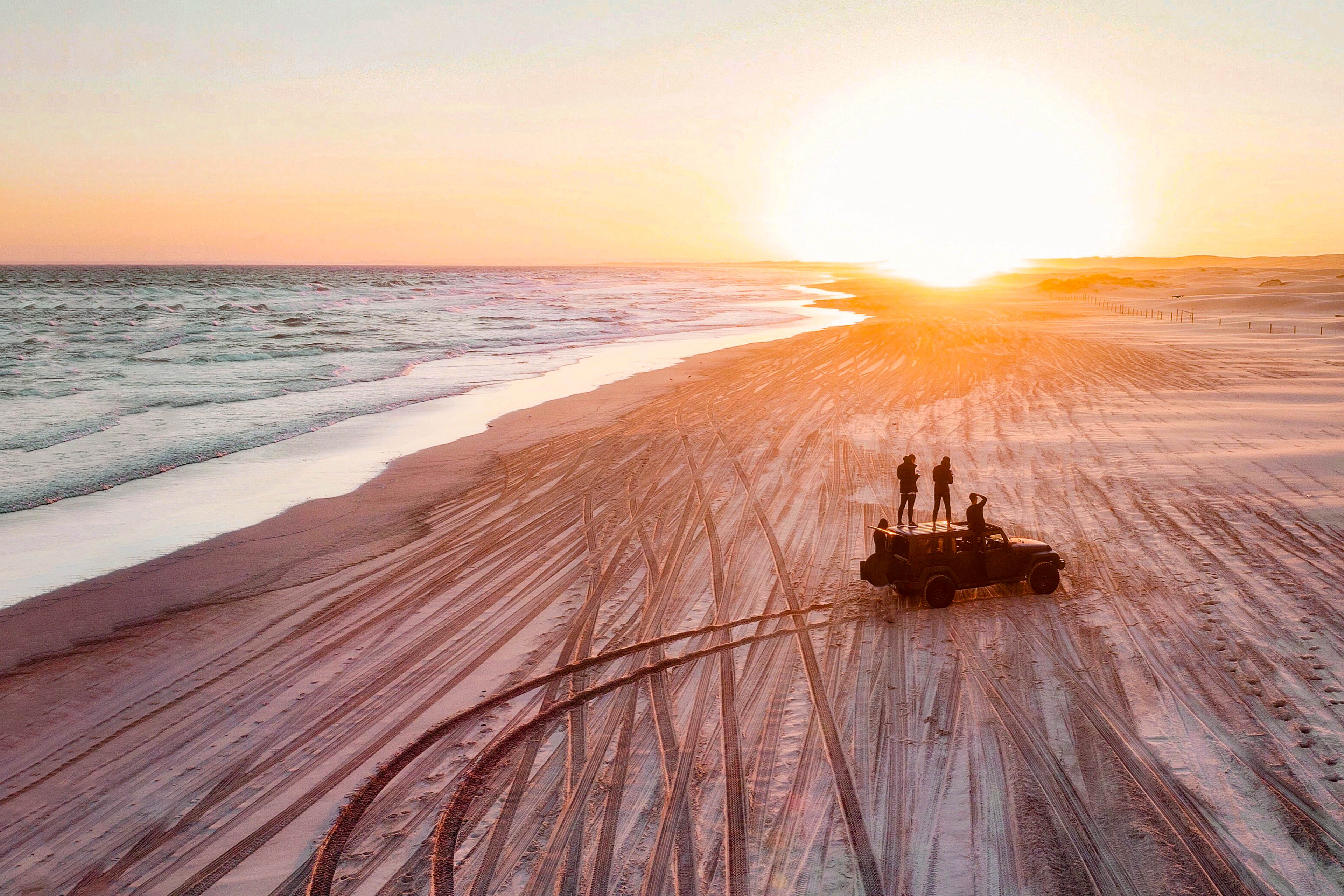 mensen kijken naar de zonsondergang met een 4x4 op het strand