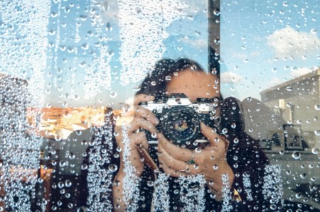 Persona fotografiando a través de gotas de lluvia en la ventana