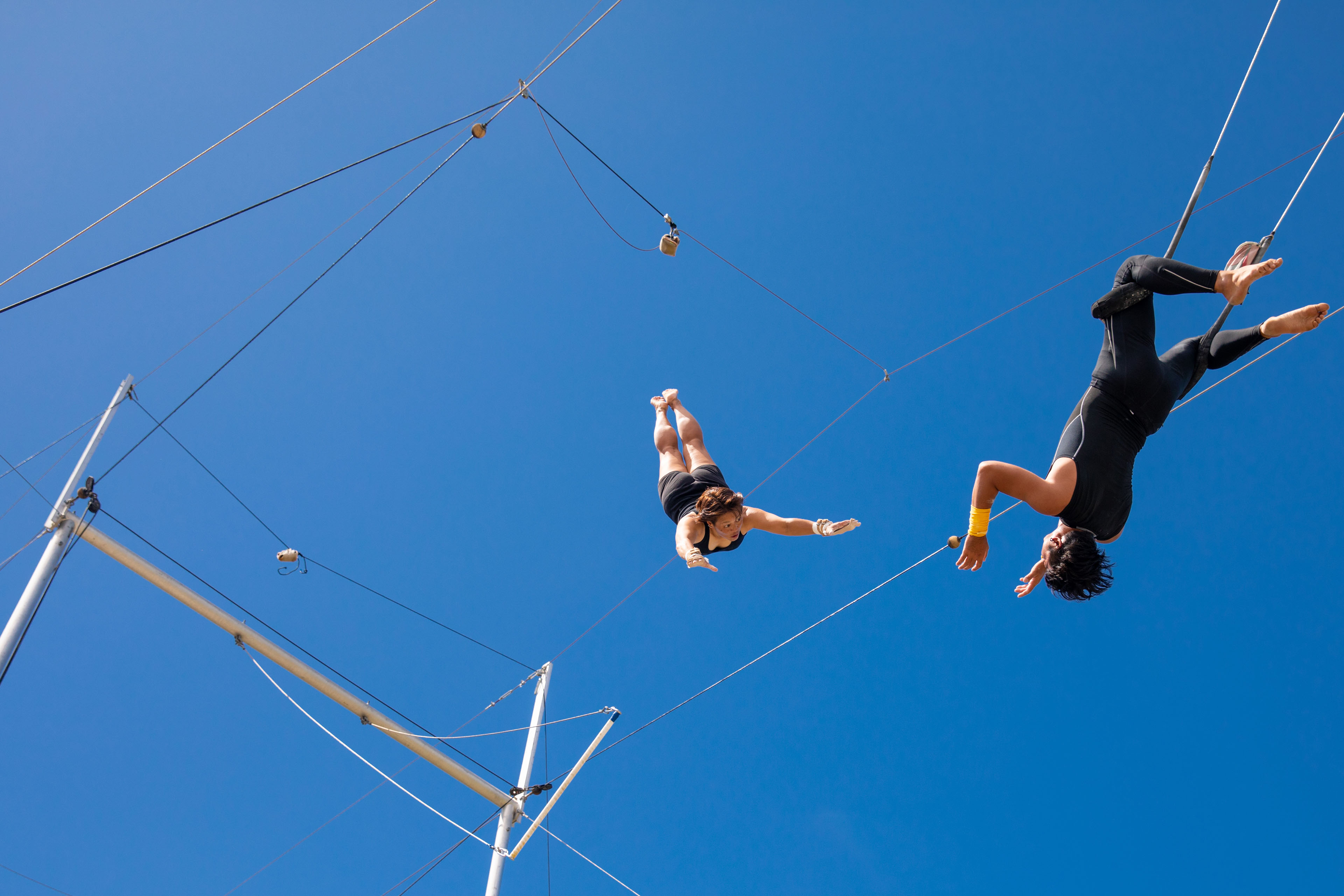 Trapeze artists practicing against the blue sky
