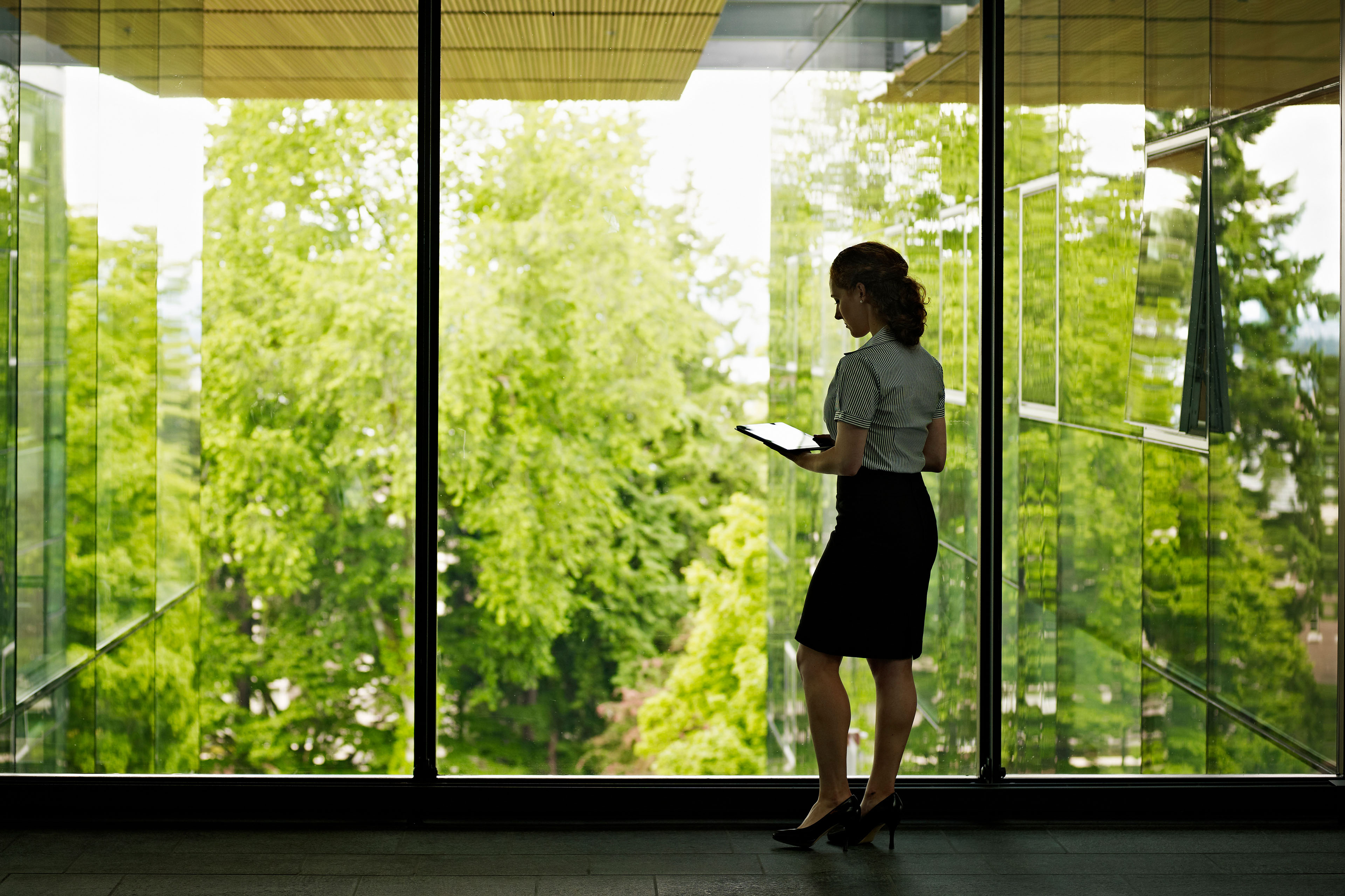 Businesswoman holding tablet standing at windows looking over green space