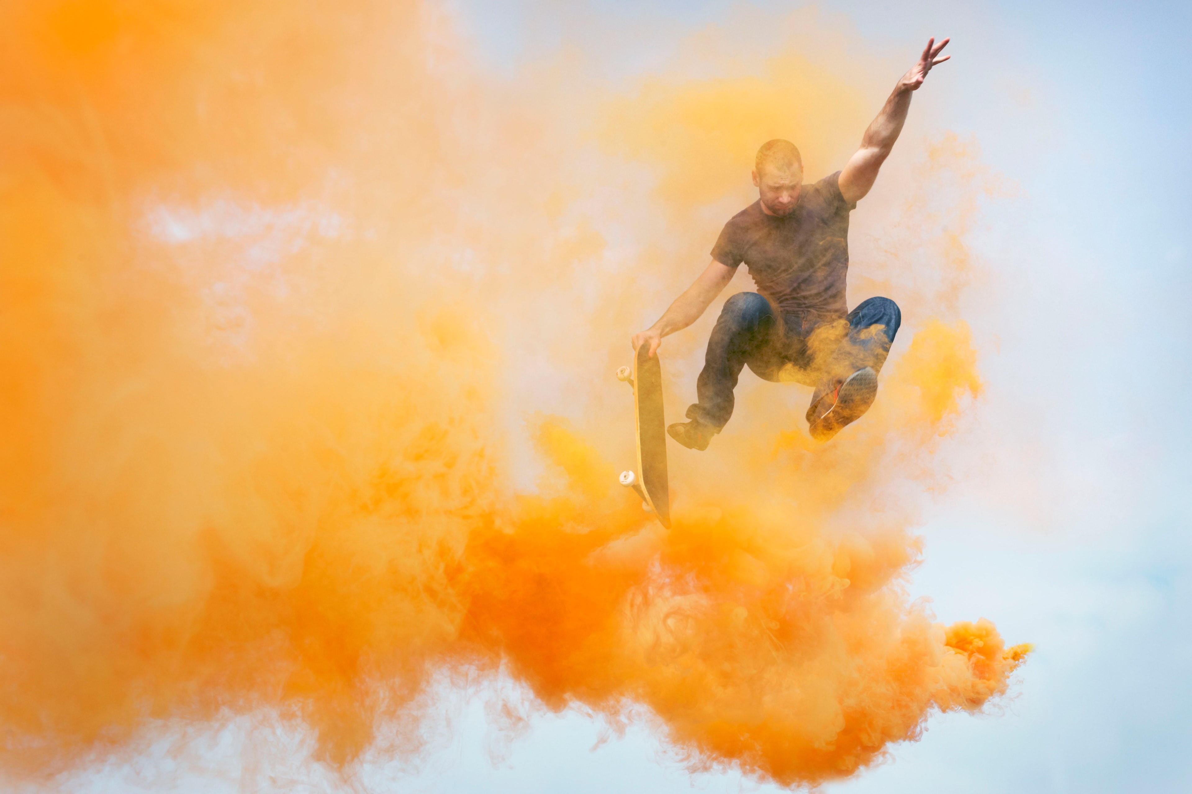 man jumping through orange smoke with skateboard