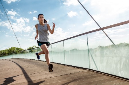 Female athlete running bridge against sky
