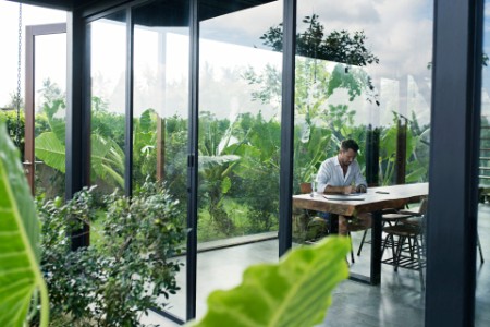 mature man sitting at table in front of lush garden writing