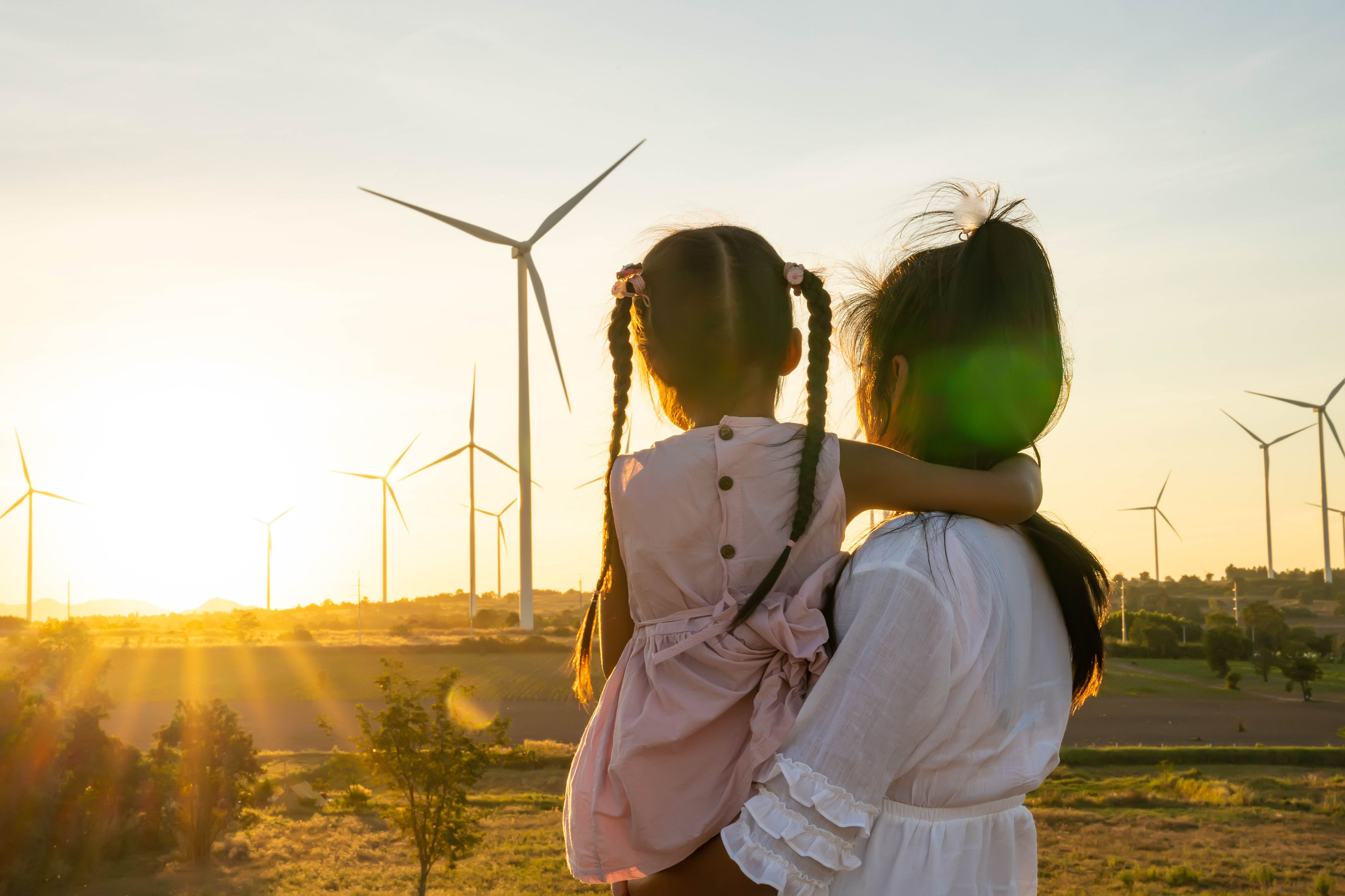 Mother and daugher look at wind turbines at sunset