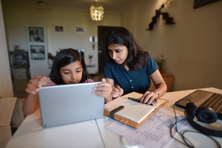 Woman working from home while daughter using digital tablet
