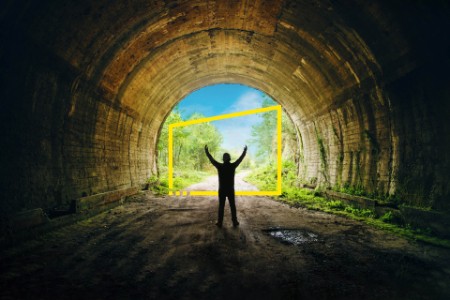 A young man stands with arms wide open against the exit of a dark tunnel
