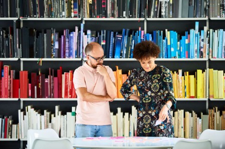 Mann og kvinne står foran bokhylle med fargekoordinert bøker