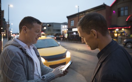Two men looking at mobile phone in front of a taxi