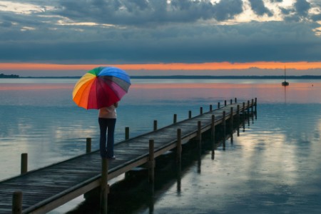Rear view on woman with multi colored umbrella in rain on lakeside jetty
