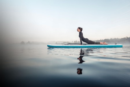 Woman practicing paddle board yoga on lake Kirchsee in the morning Germany