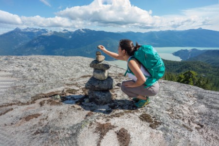 Young Woman Hiker Placing Rock on a Mountain top