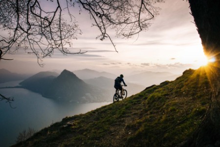 Mountain biker traverses steep mountain slope above lake