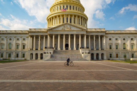 Single person riding by the back of the US Capitol building