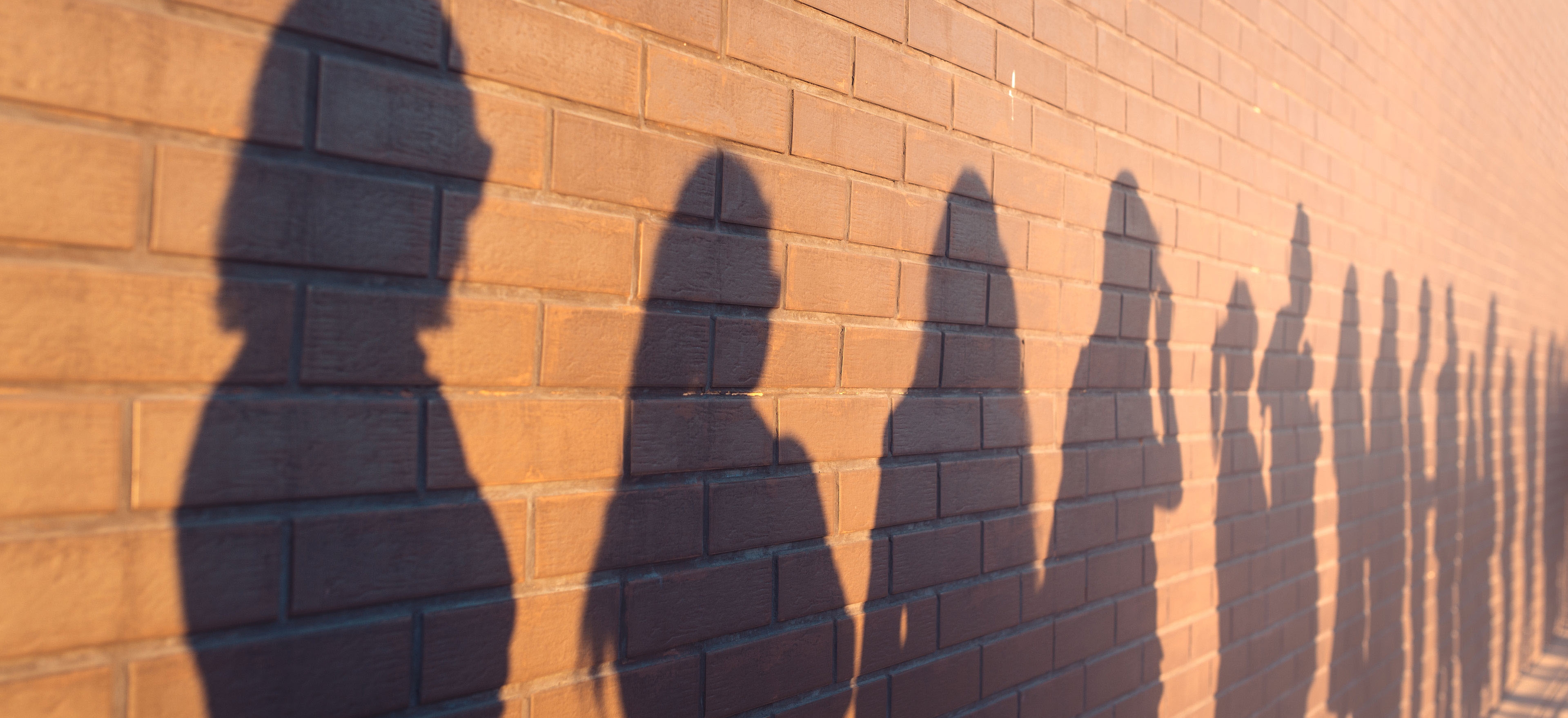 Line of shadows of people lined up against a red brick wall.